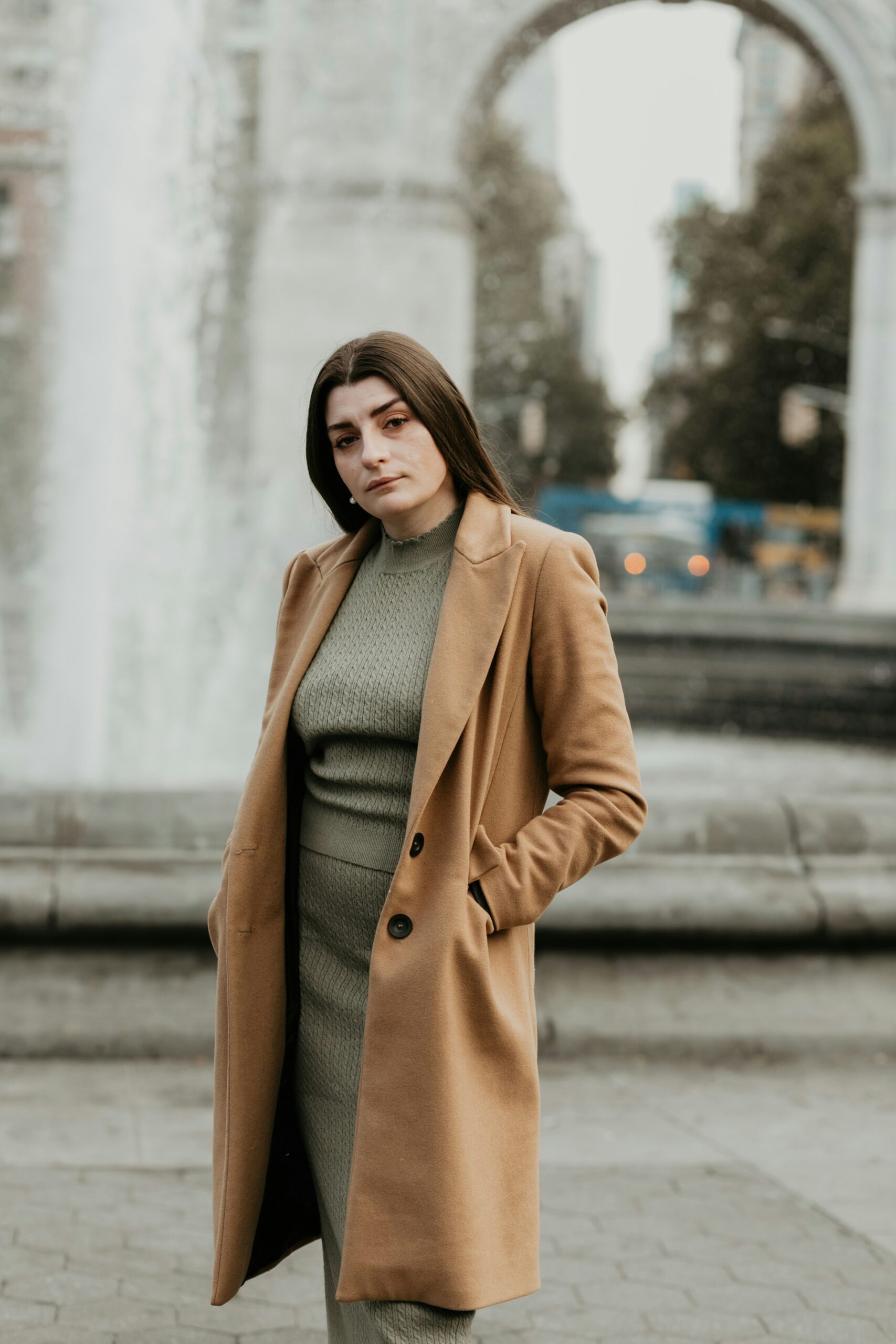 woman in brown coat standing on sidewalk during daytime